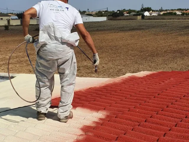 Operario aplicando la capa de acabado rojo con protección solar sobre la espuma de una cubierta de teja