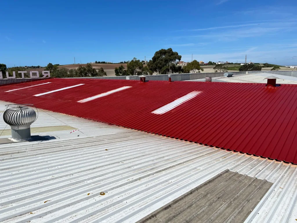 Cubierta de nave industrial impermeabilizada con acabado rojo, junto a la parte aún sin tratar