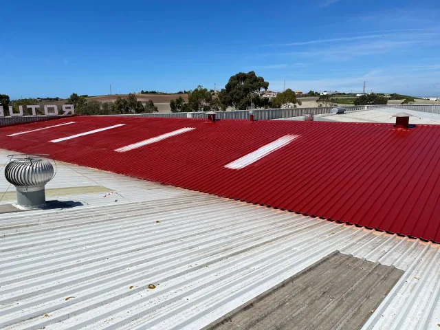 Cubierta de nave industrial impermeabilizada con acabado rojo, junto a la parte aún sin tratar