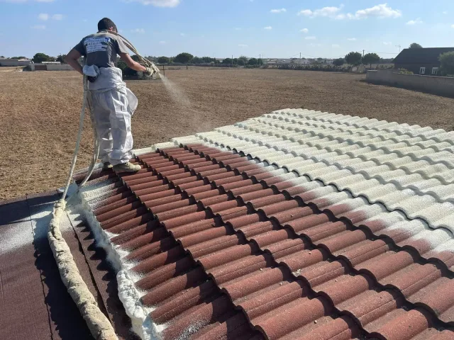 Operario proyectando poliuretano sobre la cubierta de teja de hormigón de una vivienda
