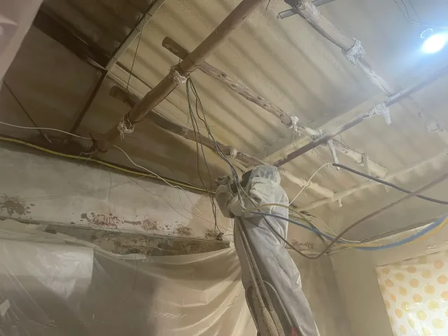 Aplicador con mono de protección proyectando poliuretano por el interior, bajo una cubierta de chapa