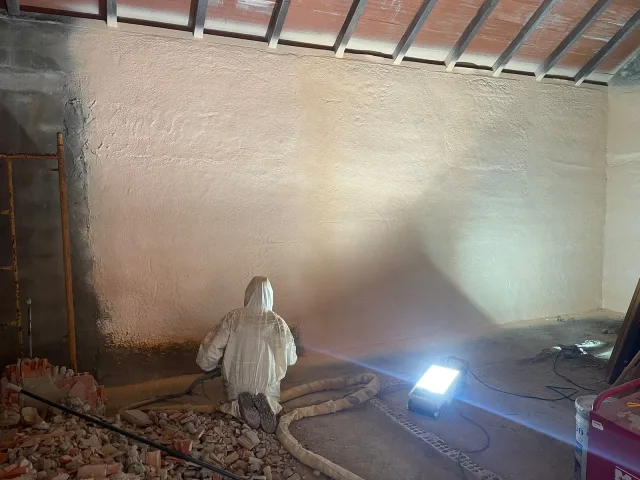 Proyección de poliuretano sobre la pared interior de una nave, iluminada con foco de obra